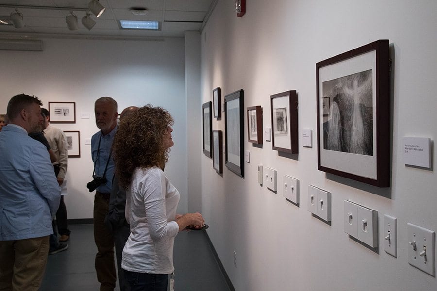 Individuals look at art pieces from the "When Man to Man is Wolf" exhibit at College of Canyons.  Photo Courtesy of Juan Renteria