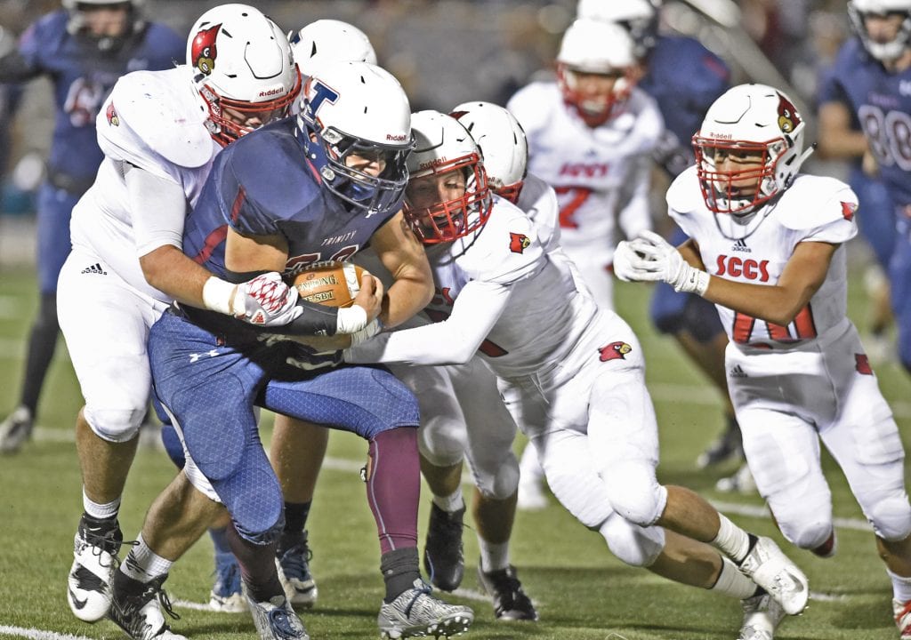 Trinity's Caden Kulp (22) is smothered behind the line of scrimmage by Josiah Park, left, and Aidan Espinosa of SCCS at Canyon High on Saturday. Dan Watson/The Signal