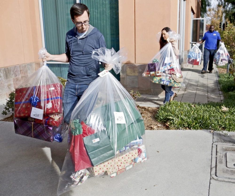 Ryan Winsor, Tamzin Horswill, both of Princess Cruises, and Ron Dale of Camelot carry bags of gifts to a moving truck before they're moved to Single Mothers Outreach on Friday. Princess Cruises has been running its Adopt-a-Family program since 2010, and donated $15,000 worth of gifts to nearly 100 families every Christmas. Katharine Lotze/Signal