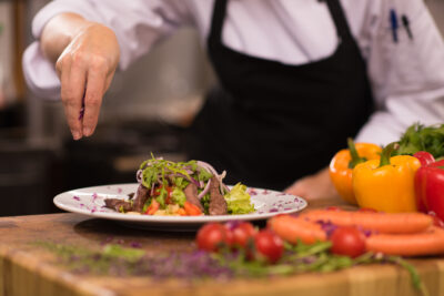 cook chef decorating garnishing prepared meal dish on the plate in restaurant commercial kitchen