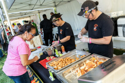 Debbie Medina, left, is served hot chicken sliders by Michael and Matthew Ungamrung, the owners of Crazy Hot Chicken, at their food booth at the Taste of the Town event at Blomgren Ranch in Santa Clarita, Calif., on Sunday, May 1, 2022. Chris Torres/The Signal
