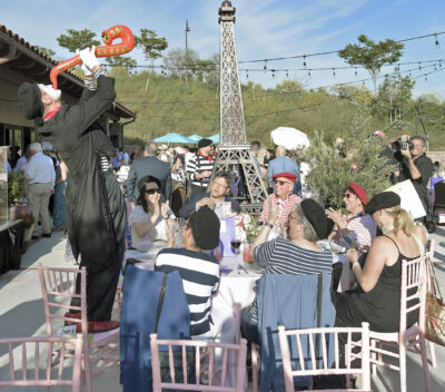 Derek Loughran as "Derek the Mime", left, plays an inflatable saxophone on a chair at the Head Table Sponsor - Home Instead during the Celebrity Waiter Dinner with the theme "Springtime in Paris" and held at the Santa Clarita Valley Senior Center at Bella Vida on Saturday, 042923.