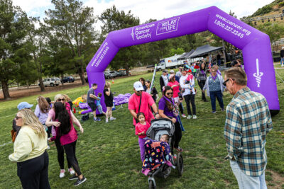 Event attendees walk under the finish line together during the Relay For Life of the Santa Clarita Valley 25th Anniversary Year event at Central park in Saugus, Calif., on Saturday, May 6, 2023.