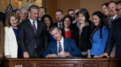 Gov. Gavin Newsom is surrounded by lawmakers as he signs into law his oil profit penalty plan in Sacramento on March 28, 2023. Photo by Miguel Gutierrez Jr., CalMatters