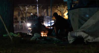 A man warms his hands near his tent in Sacramento on Feb. 24, 2022. Photo by Miguel Gutierrez Jr., CalMatters