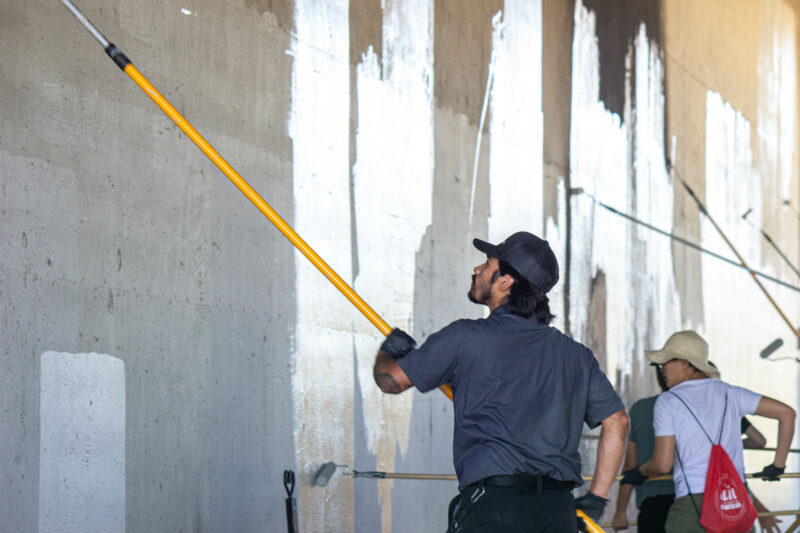 City of Santa Clarita part-time temporary seasonal worker Adrian Martinez holds up a large paint roller while painting one of the walls of the Soledad Canyon Road overpass on Saturday morning during the third annual Graffiti Removal Day on Aug. 3, 2024. Trisha Anas/ The Signal.