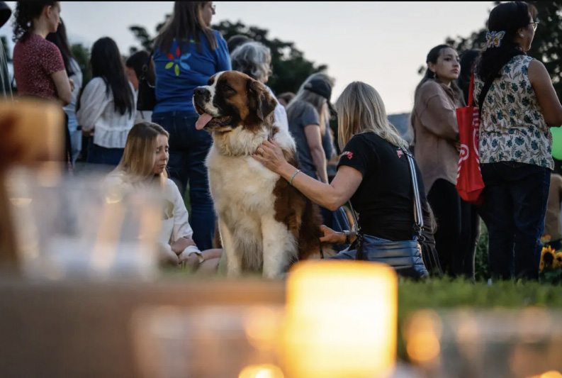 Kate Campo (R), a business owner in the neighborhood, sits with her dog, joining others in mourning the two schoolchildren who were killed a day before during the Annunciation Catholic School shooting in Minneapolis on Aug. 28, 2025. Photo by Madalina Kilroy.