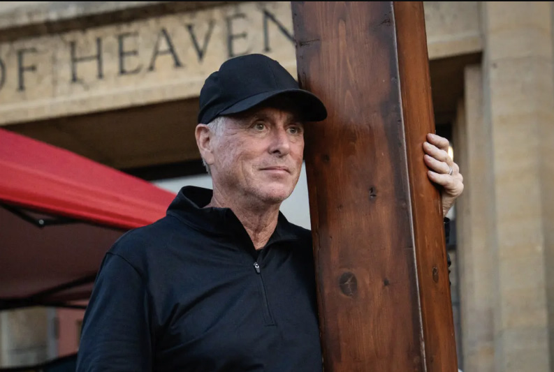 Dan Beazley drove 11 hours from his home in Detroit to bring his 10-foot-tall, 65-pound cedar cross to the Annunciation Catholic community shooting scene in Minneapolis on Aug. 28, 2025. Photo by Madalina Kilroy.