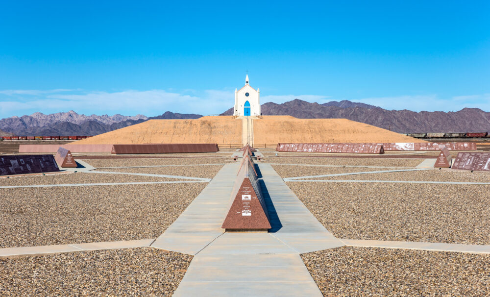 The Chapel of the Desert a small religious sanctuary situated atop a 35-foot man-made hill. The iconic cream-colored structure with its turquoise blue door stands out against the muted colors of the desert. ©SHUTTERSTOCK