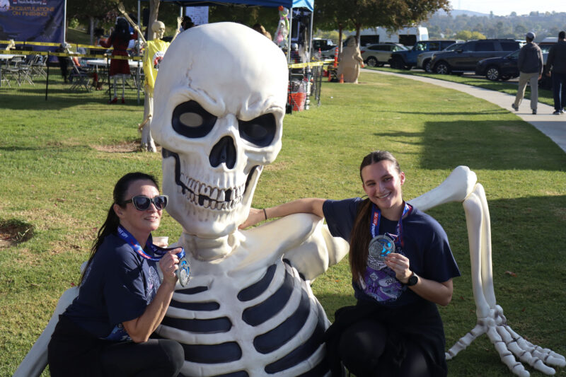 Shirley Hart (L) and Boden Bartholomew (R) smile with a spooky friend and show off their medals at the "Finish the Ride and Finish the Run" event at West Creek Park in Valencia, Calif., Sunday, Oct. 26, 2025. Kamryn Martell/The Signal