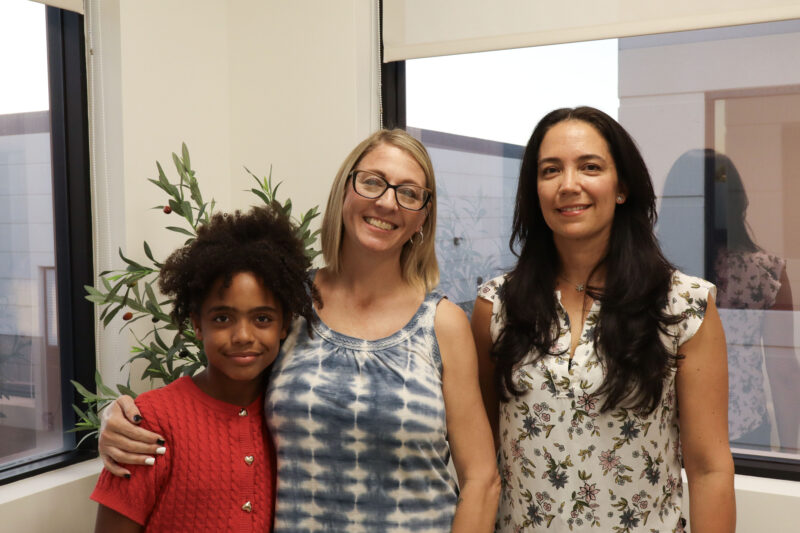 Shekainah Foster (L), 10, Cynthia Foster (C), and Angela Bernal (R), smile for a photo before the next group comes in to listen at the Single Mothers Outreach "Adopt-A-Family" kickoff celebration at the SMO offices in Valencia, Thursday, Oct. 30, 2025. Kamryn Martell/The Signal