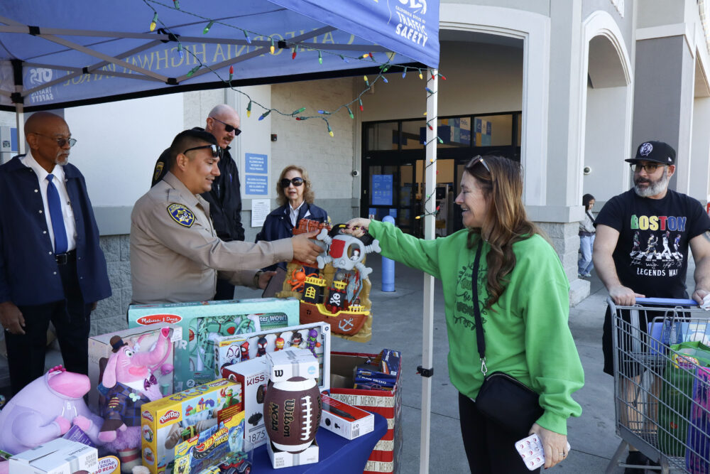 A passing Walmart customer hands her donations to Officer Carlos Burgos-Lopez (L, brown uniform) at the inaugural "Stuff-A-Bus" CHiPs for Kids toy drive at Walmart Supercenter in Valencia, Calif., Sunday, Dec. 7, 2025. Kamryn Martell/The Signal