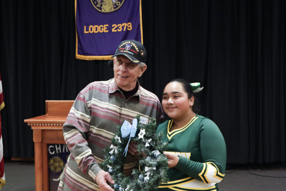 Rick Barker (L), a Marine Corps veteran, and Chandelle Brindis (R), a Canyon High School JV cheerleader, 14, smile for the camera at the Canyon High JV Cheer wreath ceremony at the Santa Clarita Elks Lodge #2379 in Canyon Country, Calif., Monday, Dec. 8, 2025. Kamryn Martell/The Signal