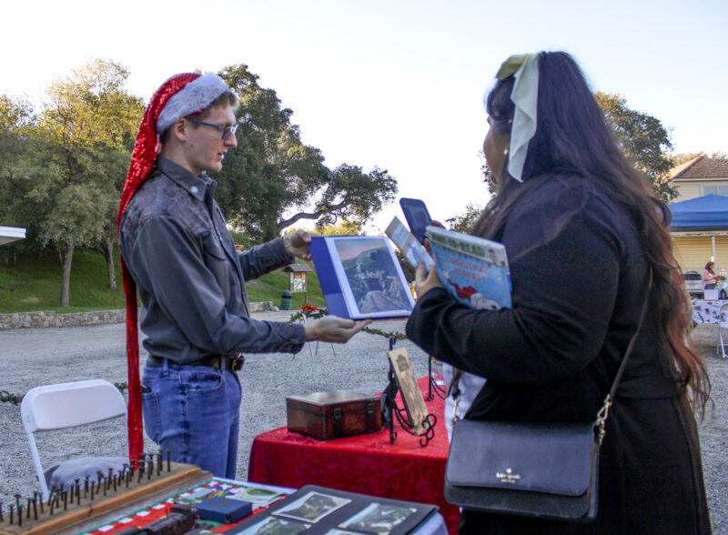 Brad Jorgensen, a Santa Clarita Valley Historical Society volunteer, shows display table items to a passerby at the nonprofit's Polar Express Experience on Saturday, Dec. 6, 2025.