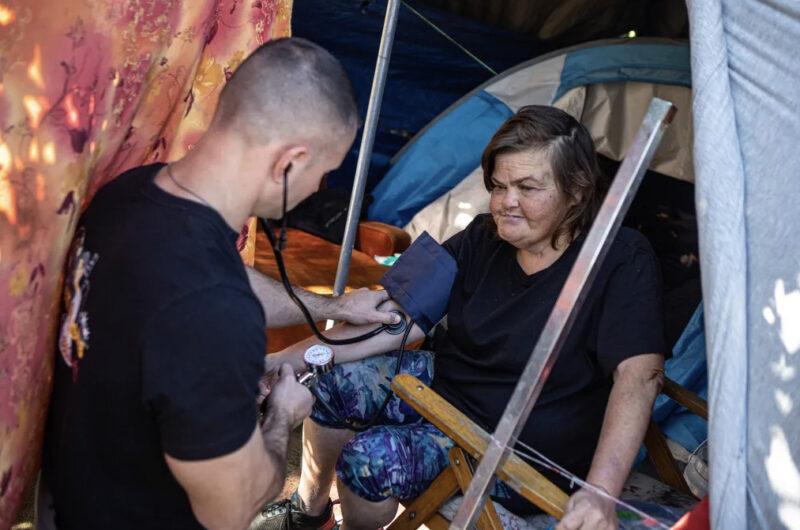 Physician assistant Brett Feldman checks Carla Bolen’s blood pressure at her encampment on the Figueroa Street Viaduct above Highway 110 in Elysian Valley Park in Los Angeles on Nov. 18, 2022. Photo by Larry Valenzuela, CalMatters/CatchLight Local