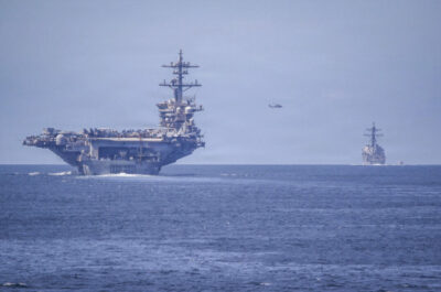 An MH-60R Sea Hawk, assigned to Helicopter Maritime Strike Squadron (HSM) 71, flies between Nimitz-class aircraft carrier USS Abraham Lincoln (CVN 72) and Arleigh Burke-class guided-missile destroyer USS Spruance (DDG 111) transiting the San Bernardino Strait in formation with Arleigh Burke-class guided-missile destroyer USS Frank E. Petersen Jr. (DDG 121) on Dec. 25, 2025. Mass Communication Specialist 3rd Class Christian Kibler/U.S. Navy.