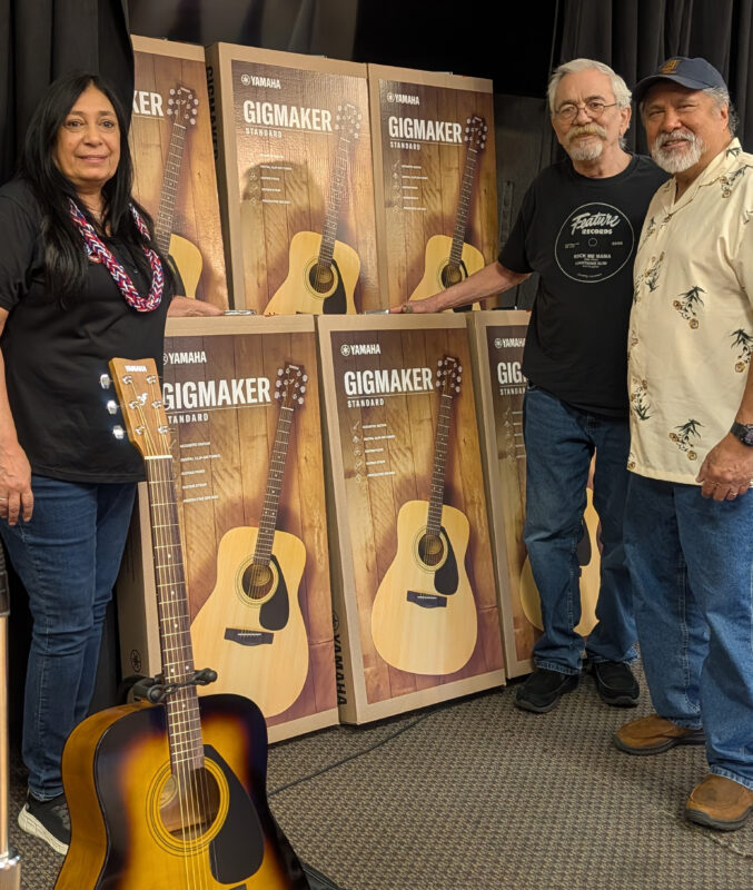 Event co-chair Jeanette Fisher presented Guitar Alliance members Tom Lamog and Bruce Geiger with seven new guitars for the group’s use. Courtesy photo.