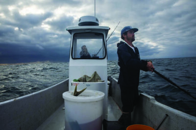Right to left, fisherman Shane Volberding and deckhand Destiny Louise Silva look off into the distance as dark clouds cover the coast of La Jolla in San Diego on May 26, 2026. Photo by Adriana Heldiz, CalMatters