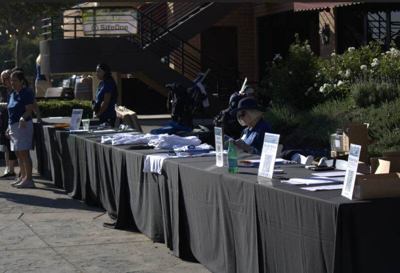 Table where guests sign in and can get free shirts and goodie bags from participating in the golf tournament at the Valencia Country Club in Valencia, Calif., Thursday, Oct, 19, 2026. Audrey De Laura/The Signal
